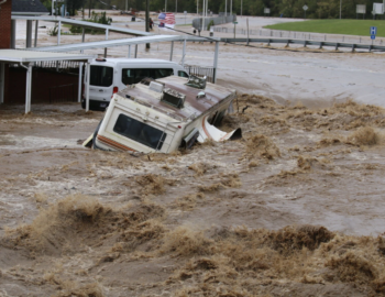 The upper half of an RV pokes up above brown floodwaters