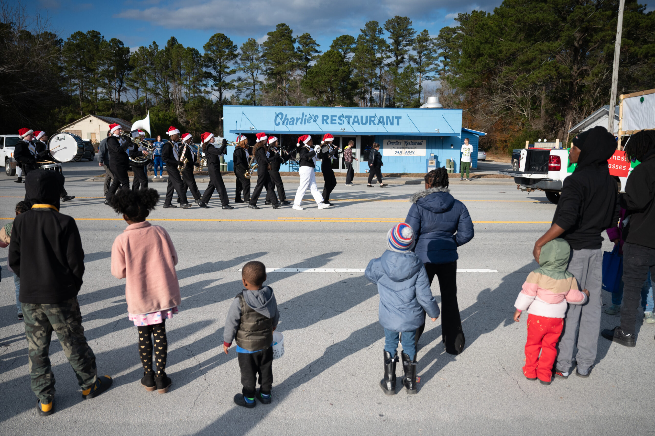 Children stand on the side of the road watching a small band march by